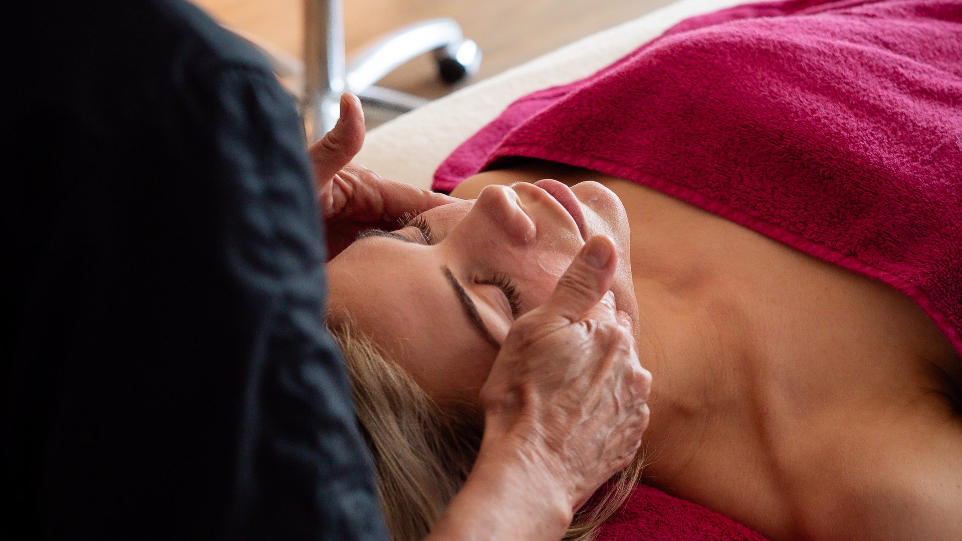 Frau erhält Gesichtsmassage in einem Spa auf einem roten Handtuch