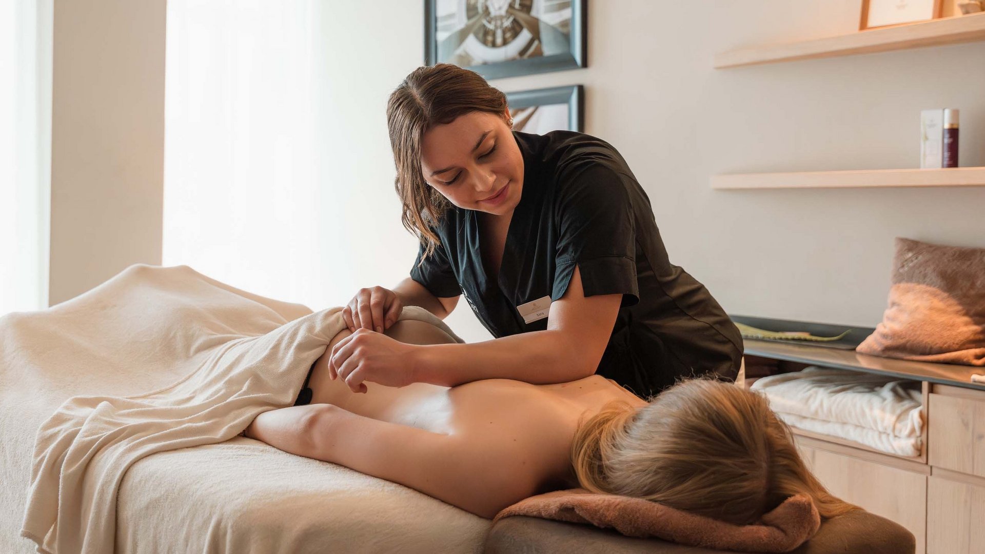 Schenna Resort Frau bekommt Rückenmassage in einem hellen Massagezimmer