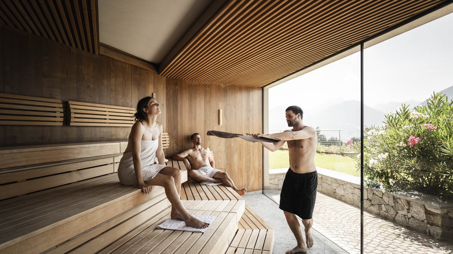 People relaxing in a sauna with wooden walls and large window overlooking garden