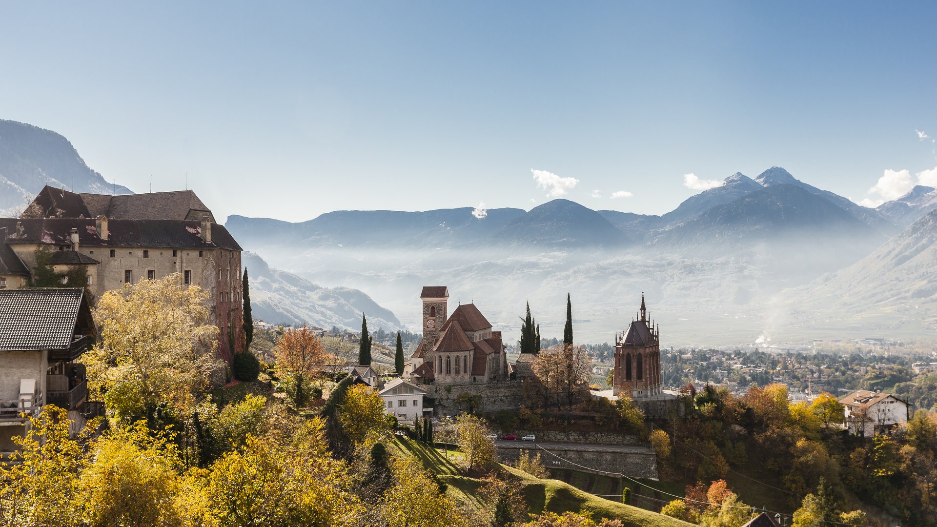 Historisches Dorf mit Burg und Kirche vor nebligen Bergen im Herbst