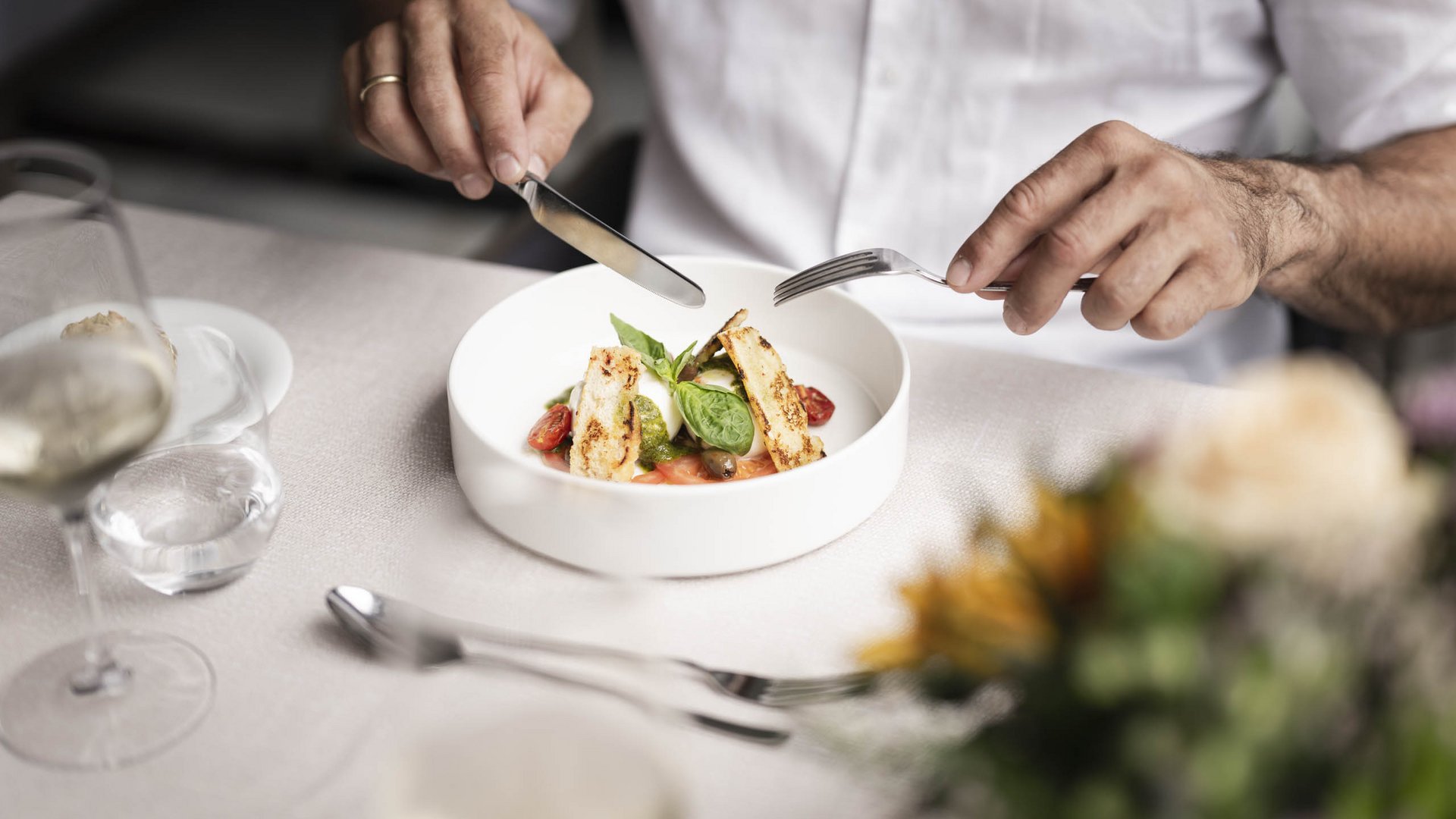 Person schneidet ein Gericht mit Tomaten und Basilikum in weißer Schüssel an