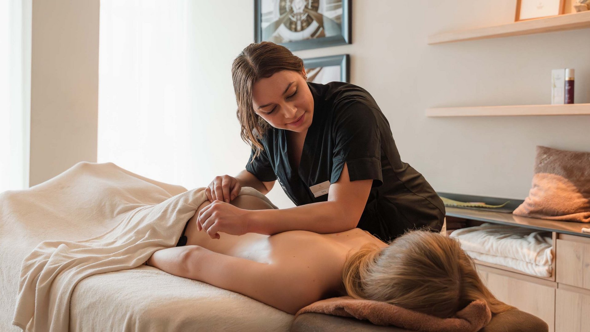 Schenna Resort Frau bekommt Rückenmassage in einem hellen Massagezimmer