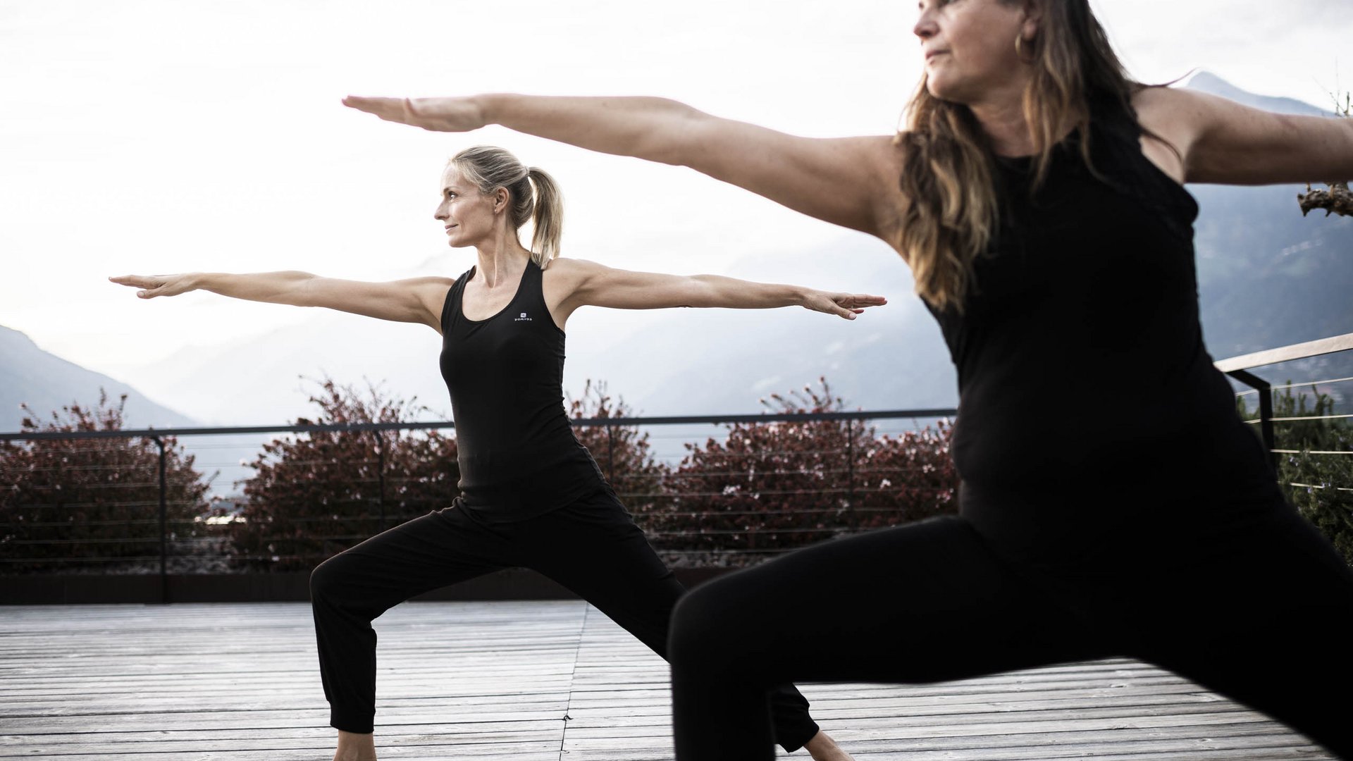 Schenna Resort Zwei Frauen praktizieren Yoga im Krieger-Posen auf einer Terrasse mit Bergblick