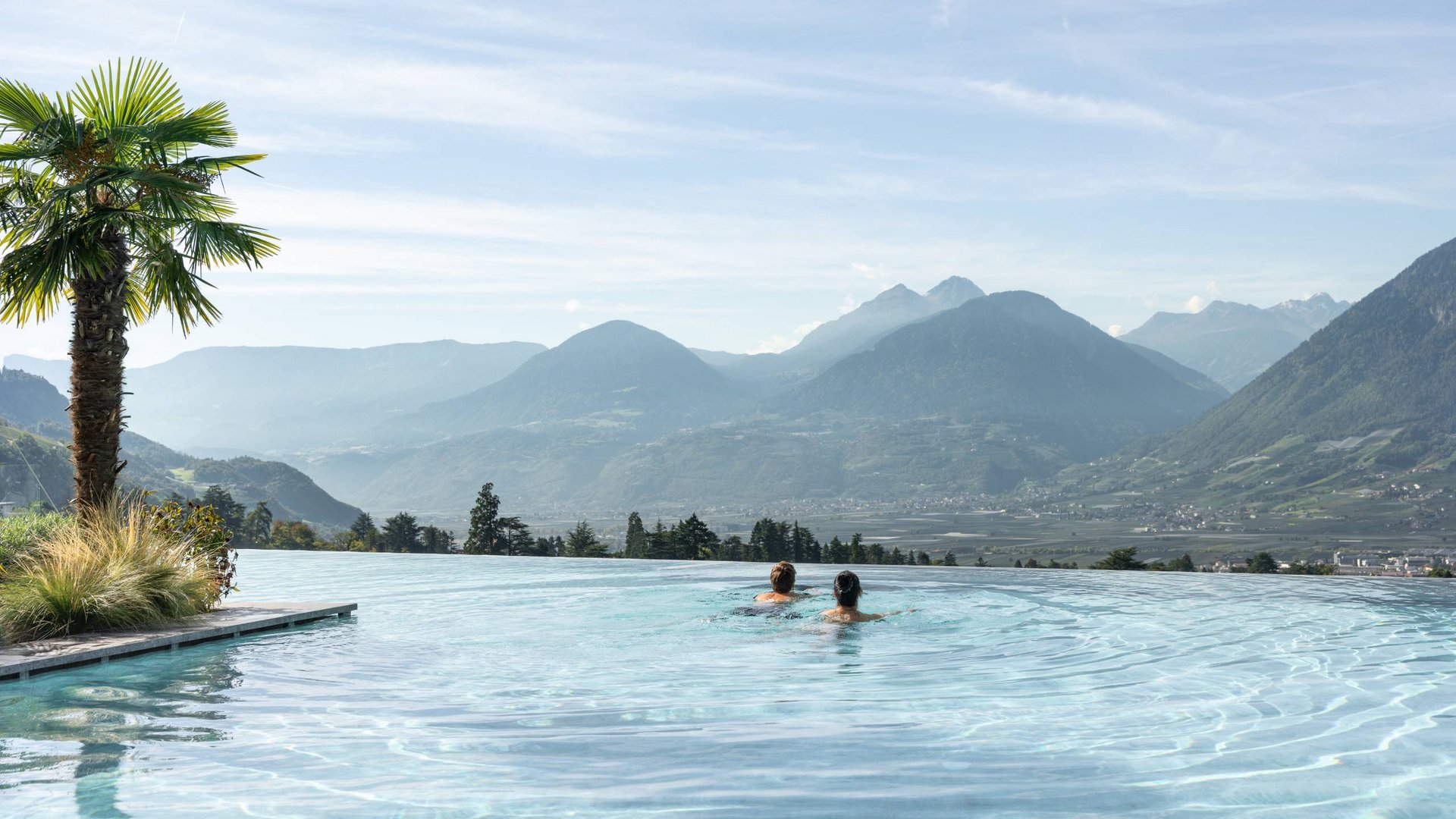 Two people swimming in an infinity pool with mountain view