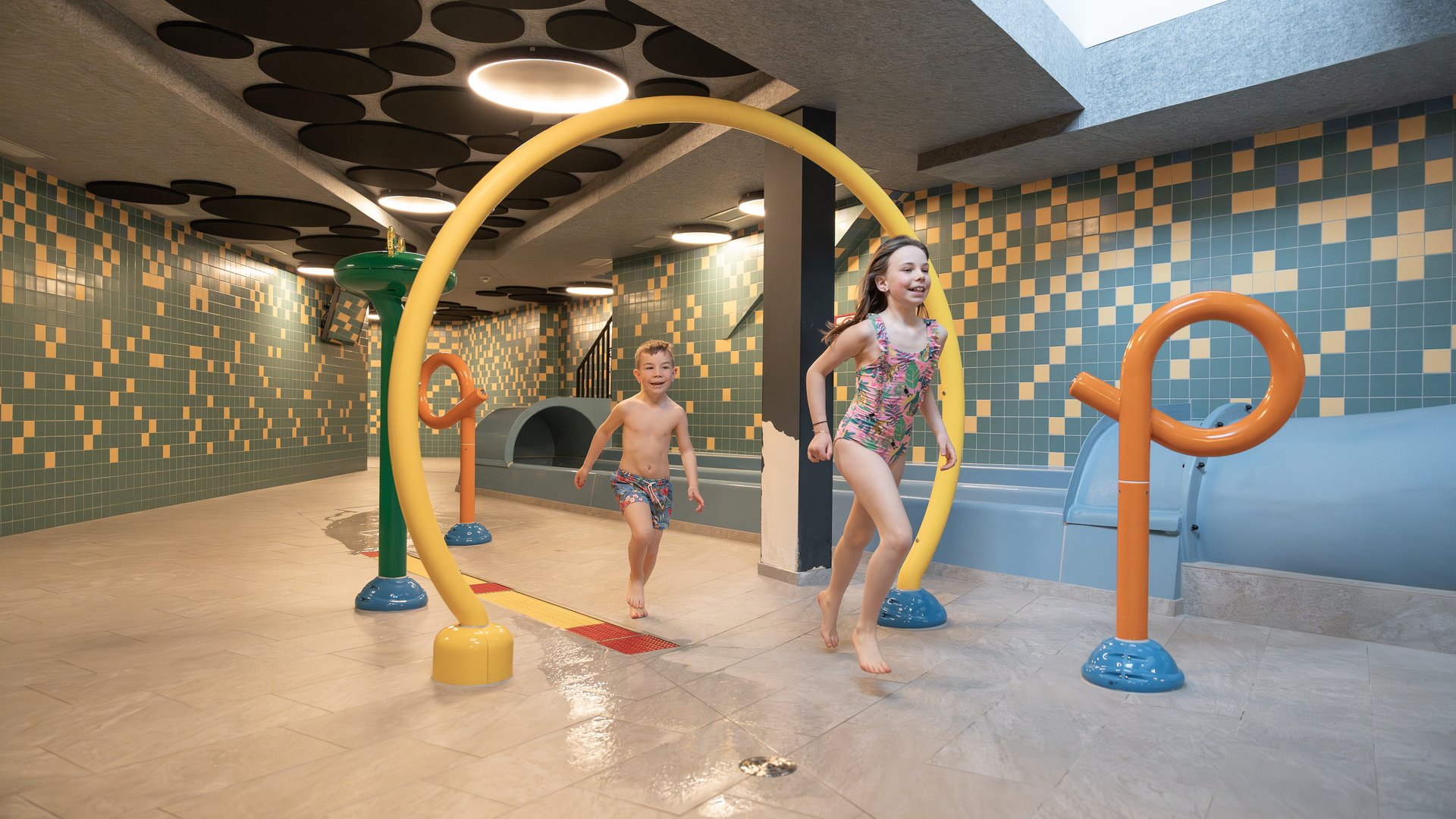 Schenna Resort Due bambini che giocano in un parco acquatico interno con giochi d'acqua colorati