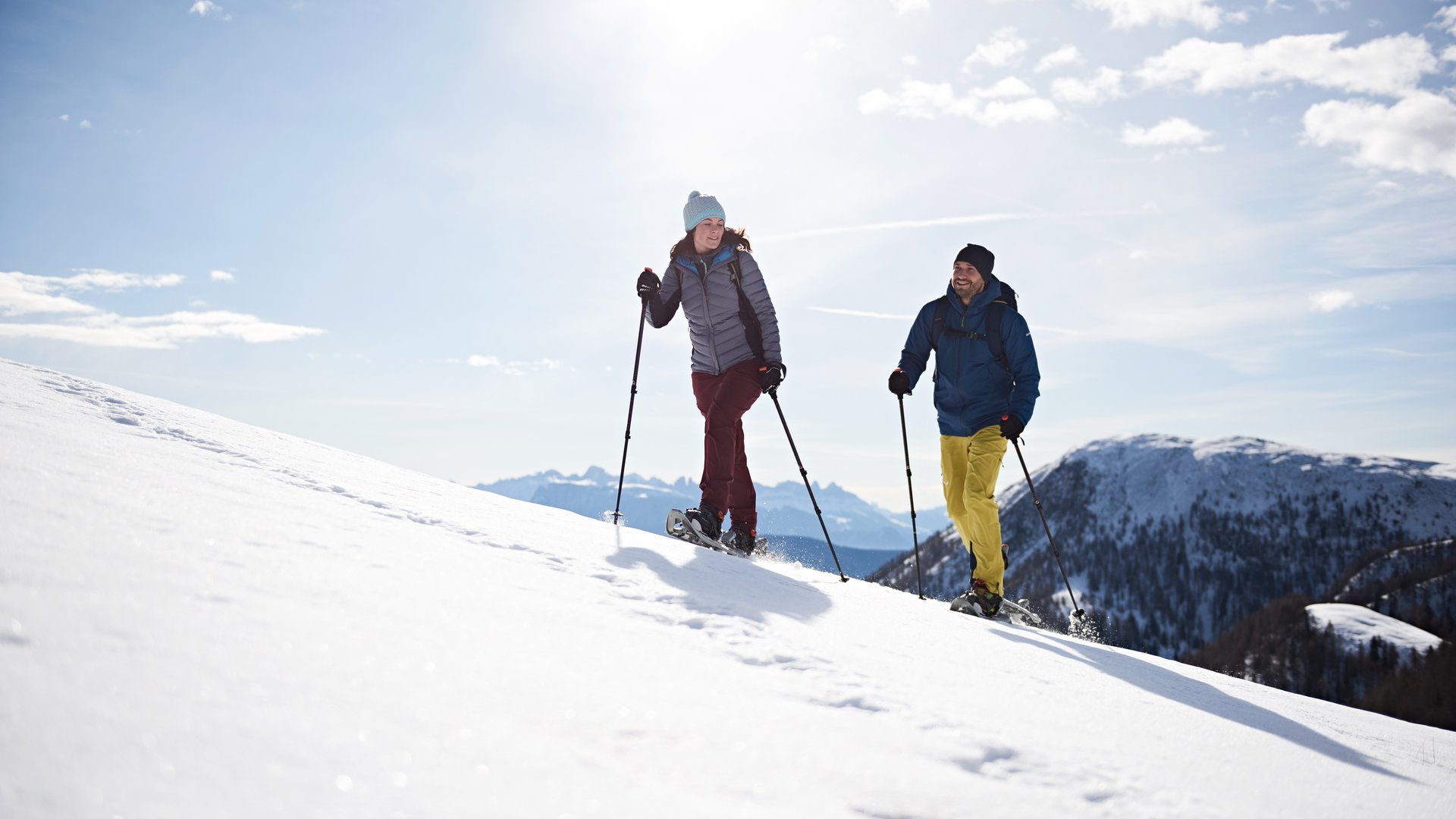 Schenna Resort Two people snowshoe hiking in the mountains on a sunny day