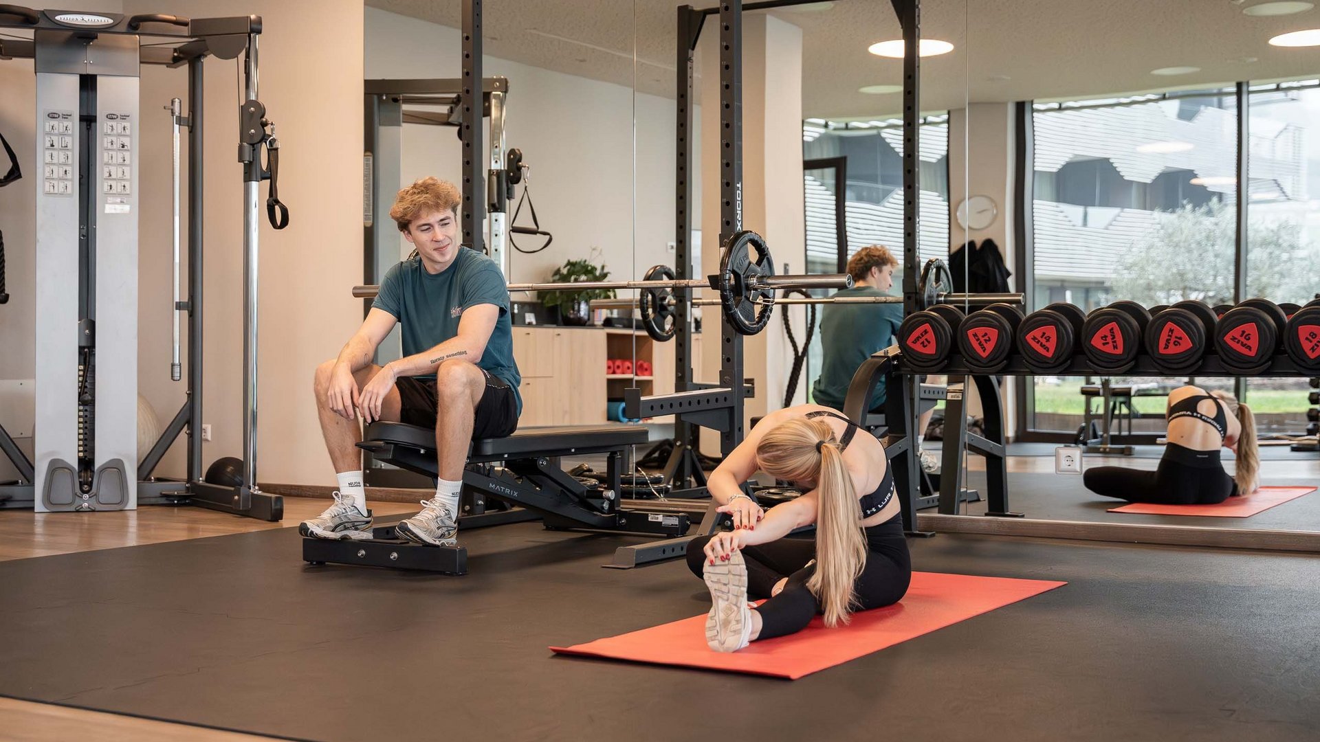 Schenna Resort Personen im Fitnessstudio beim Dehnen und Pausieren auf Matte